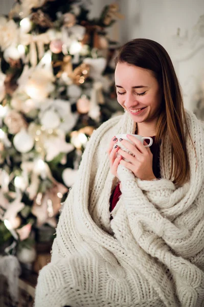 Glückliche junge Frau mit Tasse Heißgetränk am Weihnachtsbaum — Stockfoto