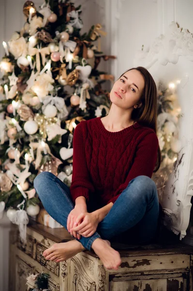 Femme avec un cadeau de Noël assis sur la commode acncient décoré pour Noël. Sapin en arrière-plan — Photo