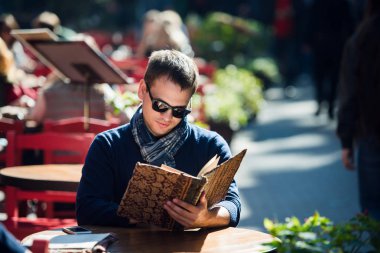 Genç yakışıklı yana doğru seyir sokak kafe sabah gazetesini okumaya giyen güneş gözlüğü adam. Kahve molası.