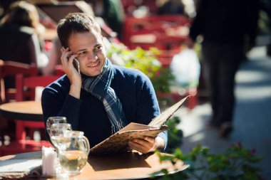 Adam kafe ile konuşmak ve bir şey sipariş smartphone üzerinde. Yakışıklı genç casual adam açık havada mutlu oturma gülümseyen hareket eden hücre telefon kullanarak.