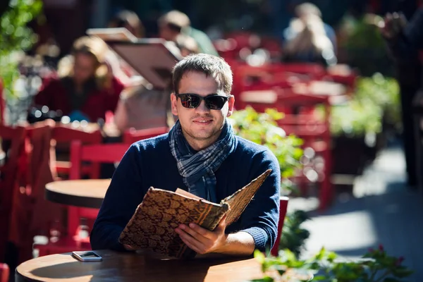 Joven hombre guapo mirando el menú al aire libre — Foto de Stock