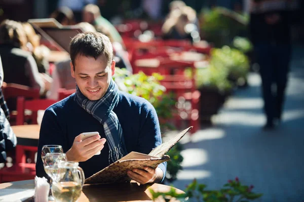男人坐在户外的街头咖啡厅检查他的手机 — 图库照片