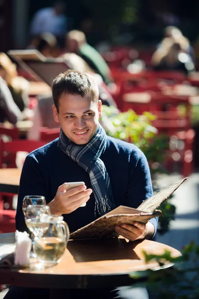 Человек проверяет свой мобильный телефон, сидя в кафе на улице — стоковое фото