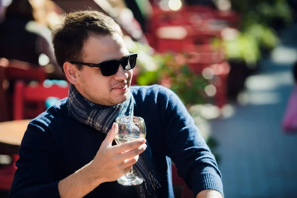 Jonge man vergadering aan buitenbar tafel met een glas witte wijn en op zoek naar camera — Stockfoto