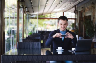 Bir fincan kahve fotoğraf çekici ve üniversite veya street Cafe'de kantinde dizüstü kullanarak genç öğrenci adam