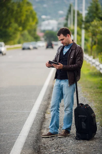 Man standing with digital tablet waiting for car or taxi. Hitchhiking — Stock Photo, Image