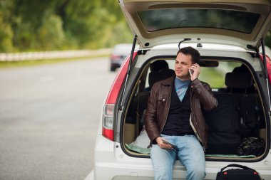 Arkadaş arıyorum. Cep telefonu konuşurken ve bir araba gövdesinde oturan mutlu genç adam