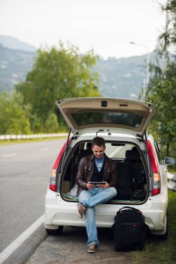 Eğlence, gezi, seyahat ve insanlar kavramı - mutlu adam online harita hatchback araba açık havada gövdede oturan tablet kullanarak konum arama