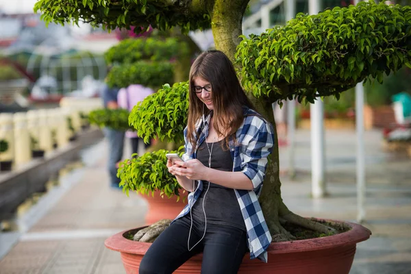 Feliz hermosa chica de secundaria caucásica joven con teléfono inteligente al aire libre en soleado día de verano mensajes de texto y sonriendo . — Foto de Stock