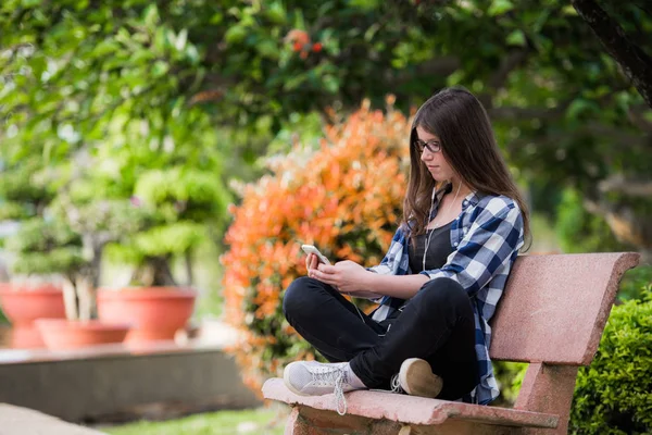 Chica feliz usando un teléfono inteligente en el parque de la ciudad sentado en el banco — Foto de Stock