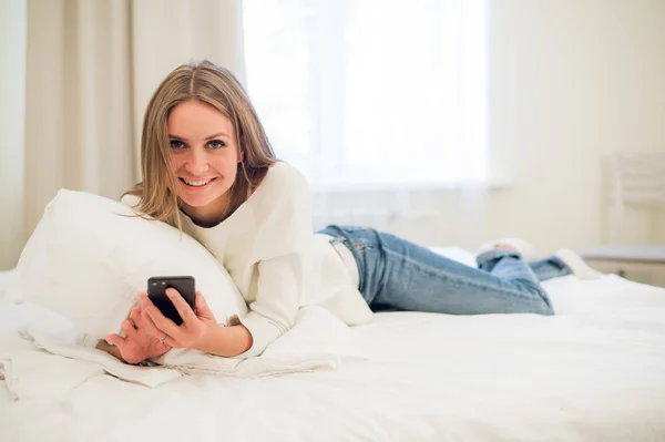 Hermosa mujer enviando un mensaje con un teléfono móvil en la cama — Foto de Stock