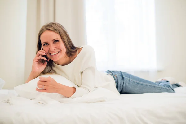 Mujer feliz sonriendo en el teléfono acostado en la cama — Foto de Stock