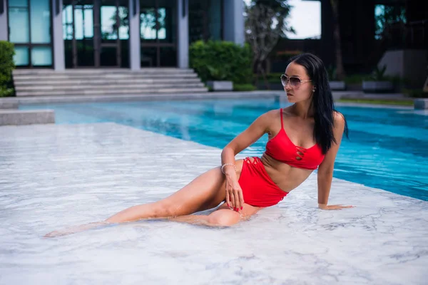 Prendere in giro giovane donna sorridente bellezza bruna con bikini rosso poggia su marmo bagnato a bordo piscina godendo l'estate nella piscina all'aperto. Stile di vita, viaggio, concetto di libertà . — Foto Stock