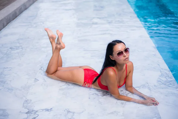 Sexig kvinna om fastställande och avslappnad nära poolen på BH bikini stekpannor, fantastisk frisyr, tan glödande hud kvinna, cool svart moderiktiga solglasögon, lång frisyr — Stockfoto