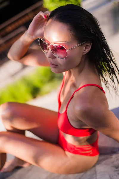 Κοντινό πλάνο Πορτρέτο γυναίκας απολαύσετε χαλαρώνοντας στην πισίνα το καλοκαίρι. Όμορφα μαλλιά μελαχρινή σέξι γυναίκα μοντέλο νεαρό κορίτσι σε γυαλιά ηλίου και κομψό κόκκινο σέξι μαγιό εσώρουχα με γύρω από την πισίνα — Φωτογραφία Αρχείου