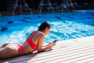 Havuz eğilerek ve cep telefonundan mesaj yazarak güzel kadın
