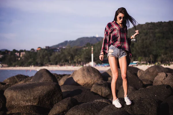 Udendørs sommer stilfuld portræt af smuk elegant kvinde med perfekt pasform krop og lange ben gå langs på stranden, bære sommer outfit, forklædt på solrig dag på stranden af sand - Stock-foto