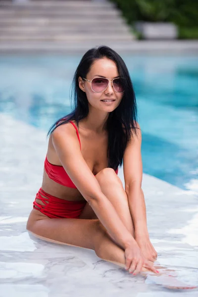 Mulher sexy elegante no biquíni vermelho no corpo magro e bem torneado bronzeado do sol está posando perto da piscina — Fotografia de Stock