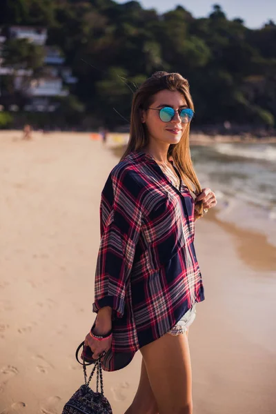 Summer sunny lifestyle fashion portrait of young stylish hipster woman walking on beach, wearing cute trendy outfit, travel, hikes, smiling enjoy her weekends — стоковое фото