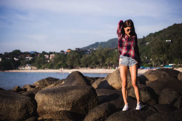 Udendørs sommer stilfuld portræt af smuk elegant kvinde med perfekt pasform krop og lange ben gå langs på stranden, bære sommer outfit, forklædt på solrig dag på stranden af sand - Stock-foto