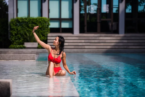 Όμορφη γυναίκα στο μπικίνι παίρνει μια selfie από δίπλα στην πισίνα σε μια ηλιόλουστη ημέρα στο πολυτελές ξενοδοχείο — Φωτογραφία Αρχείου