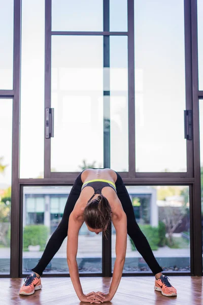 Vista trasera de la mujer joven que se extiende haciendo ejercicio matutino en el complejo hotelero de lujo con una gran vista. Modelo femenino haciendo ejercicios de flexión lateral y mirando el paisaje junto a la piscina en la ventana — Foto de Stock