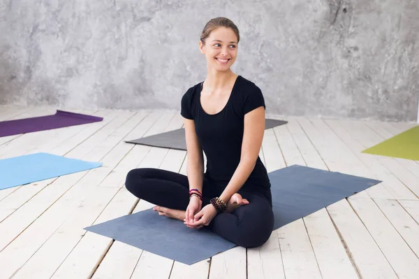 Ung attraktiv kvinna utövar yoga, sittande i Ardha Padmasana motion, halv Lotus pose, träna, klädd i svart t-shirt, byxor, meditation session på golvet vid yogaklass — Stockfoto
