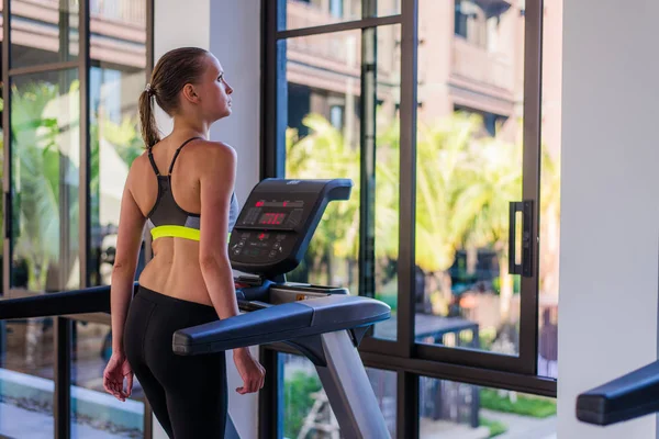 Colpo orizzontale di donna che fa jogging sul tapis roulant al centro benessere del resort di lusso. Allenamento femminile in palestra su un tapis roulant con una splendida vista estiva presso la spa dell'hotel durante l'estate — Foto Stock