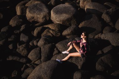 Kot pantolon seksi kadın genel ve pembe tişört rock plaj deniz okyanus sahilinde büyük taş oturamaz. Modern hippi kız iyi eğlenceler. İyi güneşli yaz gün
