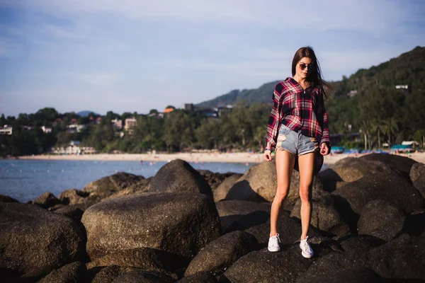 Udendørs sommer stilfuld portræt af smuk elegant kvinde med perfekt pasform krop og lange ben gå langs på stranden, bære sommer outfit, forklædt på solrig dag på stranden af sand - Stock-foto