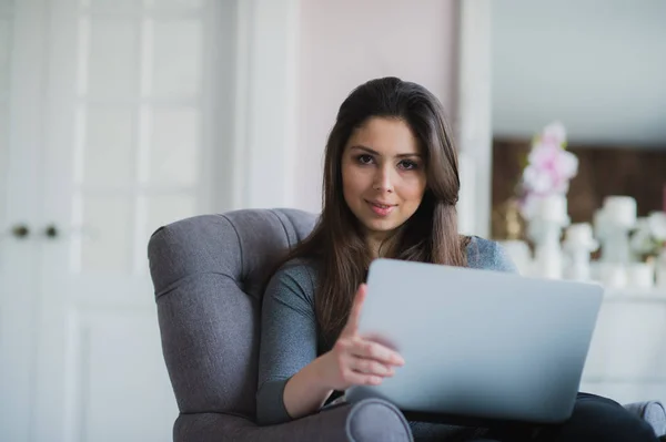 Young woman in modern luxury apartment, sitting comfortable in armchair holding computer on her laps, relaxing, working at home. eBook author, remote technical support. Lifestyle — Stock Photo, Image