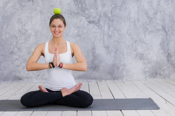 Leende kvinna gör yoga pose anläggning apple på hennes huvud — Stockfoto