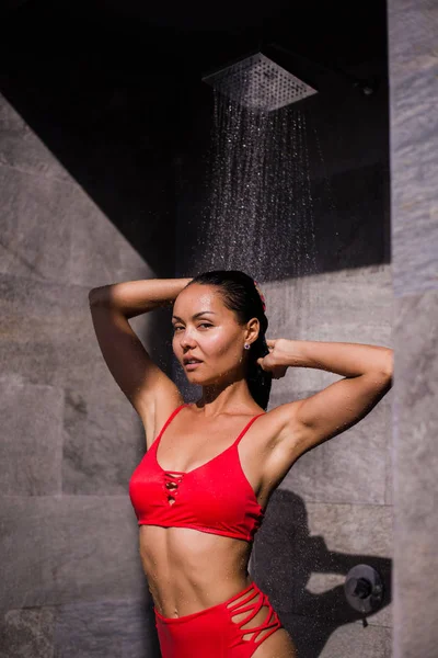 Una joven mujer sexy con traje de baño rojo duchándose afuera en un hotel de lujo — Foto de Stock