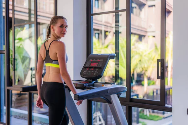 Horizontal shot of woman jogging on treadmill at health sport club at luxury resort. Female working out at a gym running on a treadmill with a great summer view at spa facility at hotel during summer