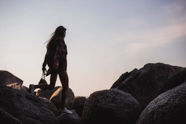 Όμορφη λεπτή γυναίκα στο πουκάμισο και σορτς μόδας γυαλιά ηλίου με τα πόδια στα μεγάλα βράχια. Θέα από το πίσω μέρος. Χαριτωμένο κορίτσι ομορφιά σε μια τροπική παραλία ωκεανού ακτή με μεγάλες πέτρες. Τρόπου ζωής καλοκαίρι υπαίθρια. — Φωτογραφία Αρχείου