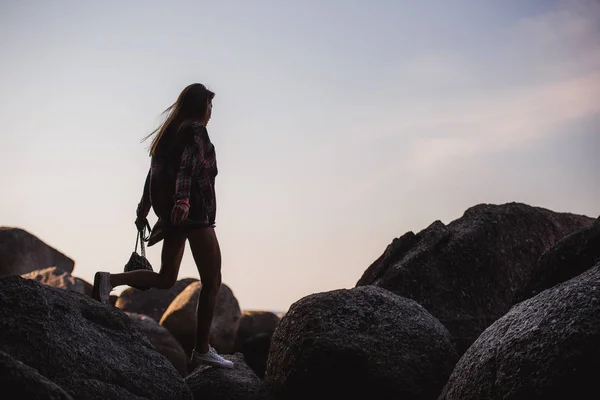 Bella donna magra in camicia, pantaloncini e occhiali da sole di moda camminare su grandi rocce. Vista da dietro. Bellezza ragazza carina su una spiaggia tropicale mare oceano riva con grandi pietre. Stile di vita estivo all'aperto . — Foto Stock