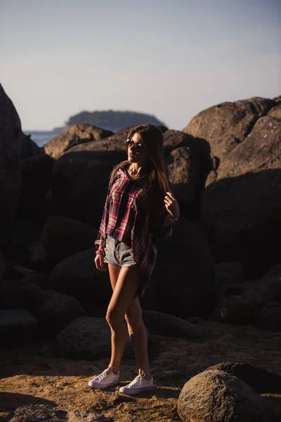 Piękna kobieta slim w koszulkę, spodenki i moda okulary przeciwsłoneczne chodzić na duże skały. Widok z tyłu. Uroda Ładna dziewczyna na tropikalne plaża shore ocean morze z dużych kamieni. Letni odkryty życia. — Zdjęcie stockowe