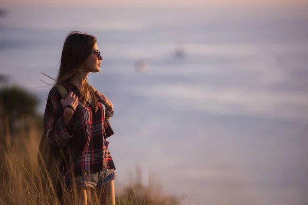 Femme voyageur regarde le bord de la falaise sur la baie de la mer des montagnes en arrière-plan au coucher du soleil — Photo