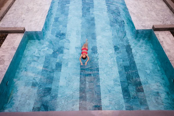 Foto aerea vista dall'alto di un modello sexy seducente in costumi da bagno bianchi sta godendo di relax in piscina durante il suo fine settimana estivo. Incredibile donna di moda in bikini con riposo spa di lusso — Foto Stock