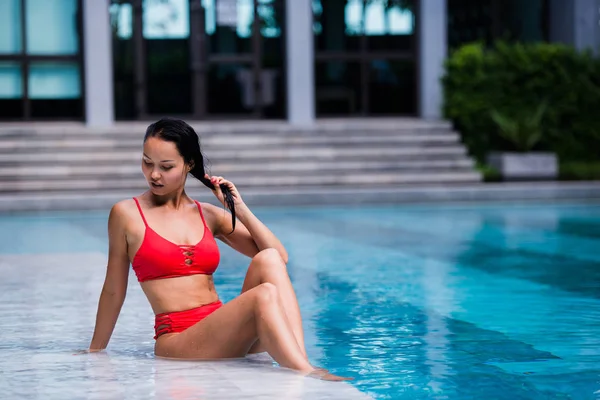 Retrato de una hermosa jovencita en bikini rojo sentada junto a la piscina en un hotel de lujo — Foto de Stock