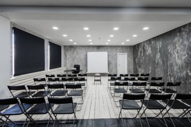 Oda bir sürü karanlık sandalye ile ders için. Duvarlar beyaz, çatı katı iç. Sağ tarafta bir kapı var. Arka plan üzerinde bir tablo ile bir dizüstü bilgisayar var.