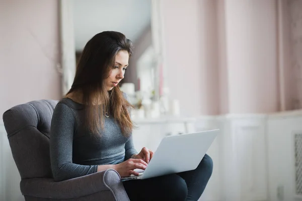 Mujer joven en moderno apartamento de lujo, sentada cómoda en sillón sosteniendo el ordenador en sus vueltas, relajante, trabajando en casa. autor del libro electrónico, soporte técnico remoto. Estilo de vida — Foto de Stock