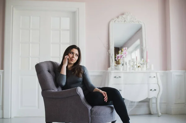 Fotografía de una mujer casual hablando con alguien en su teléfono móvil mientras está sentada en un sillón en casa . —  Fotos de Stock