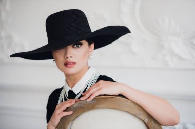 Sandalyede oturan bir şapka ile siyah elbiseli zarif kadın