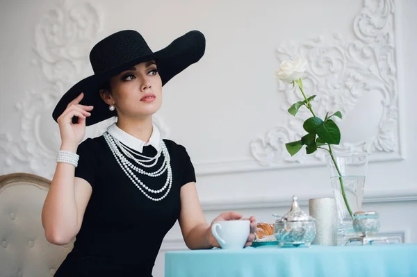 Mujer con sombrero, al igual que la famosa actriz, croissant comer y beber té . — Foto de Stock