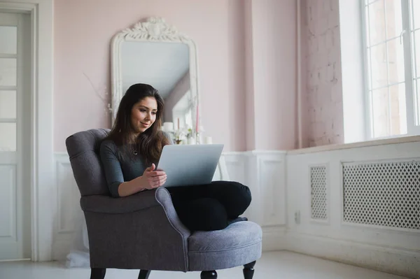 젊은 여 자가 집에서 노트북으로 그녀의 lliving 방에서 편안한 안락의 자에 — 스톡 사진