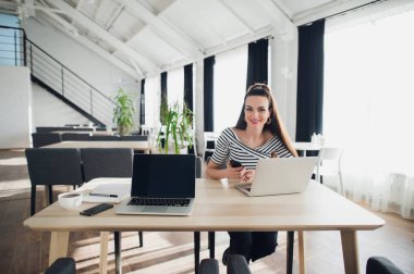 Çekici kadın çalışma Cafe içinde Laptop hakkında bir telefon tutarak gülümseyen.