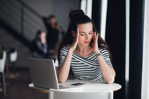 Mujer sentada en un café frente a un portátil pensando en un problema con las manos tocando la cabeza. Señora adulta tratando de encontrar una solución . — Foto de Stock
