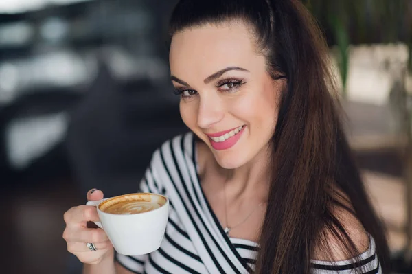 Un retrato de cerca de una mujer con una sonrisa perfecta sosteniendo una taza de capuchino o café. Dientes blancos y maquillaje . — Foto de Stock