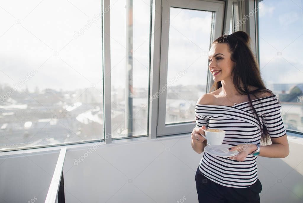 Portrait of beautiful woman smiling and looking through the window holding cup of tea.